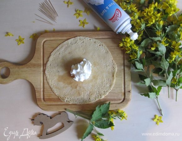 Кладем блинчик на дощечку и по центру выдавливаем взбитые сливки из баллончика.