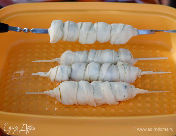 Слоёное тесто раскатать в большой прямоугольник. Толщина теста около 3 мм. Разрезать на длинные полосы шириной 3-4 см. Каждый шашлык обернуть тестом, обвивая спиралью внахлёст. Следить, чтобы не было открытых участков, иначе подтаявший сыр может вытечь. Тщательно закрепить концы теста.
