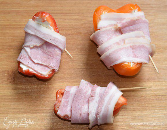 Нафаршированный перец завернуть в бекон, концы бекона закрепить зубочистками. (В дальнейшем я вынула зубочистки, т.к. запекала перцы в решетке-гриль, где овощи были надежно закреплены).