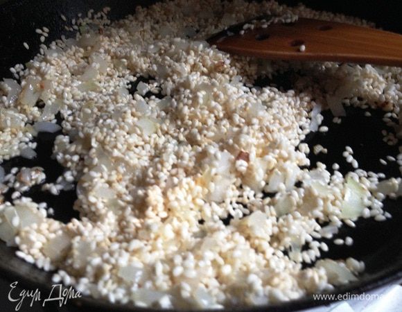 Добавить в сотейник рис. Продолжать жарить помешивая, пока рис не станет прозрачным. Добавить очищенный и измельчённый чеснок, оба вида паприки, перемешать.