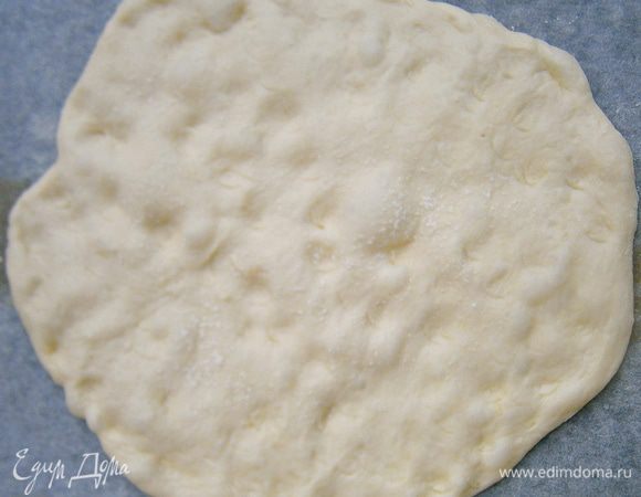 Подошедшее тесто, не вымешивая, выложить на противень (застелив бумагой для выпечки) и руками растянуть тесто в круглую лепешку.