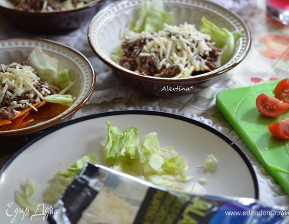 Разложить чипсы кукурузные по тарелкам. Салат нарвать, помидоры разрезать на половинки. Разложить поверх чипсов салат, затем готовый фарш с фасолью, сыр протертый.
