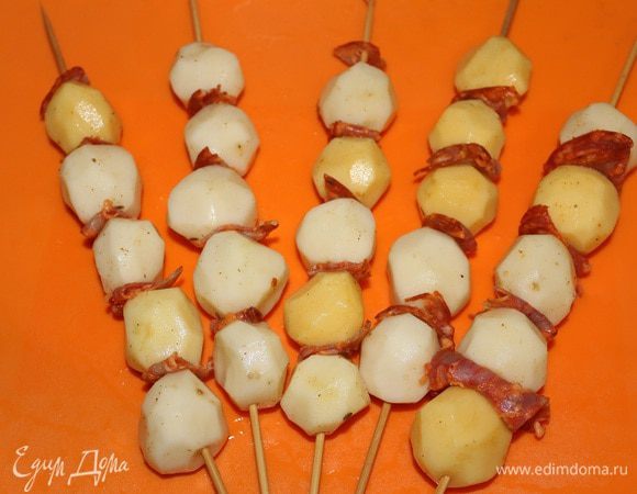 Мелкий молодой картофель очистить (лучше брать не рассыпчатые сорта картофеля). Сбрызнуть оливковым маслом и посолить. Нанизываем его на шпажки поочередно и кусочками чоризо. Пряный аромат чоризо придаст картофелю пикантный вкус, а жир который в нем содержится сделает картофель сочнее и не даст ему пересушиться. Картофель завернуть в фольгу и готовить минут 15. За это время картофель почти приготовиться и пропивается ароматом чоризо. Затем фольгу убираем и готовим его до золотистого цвета.