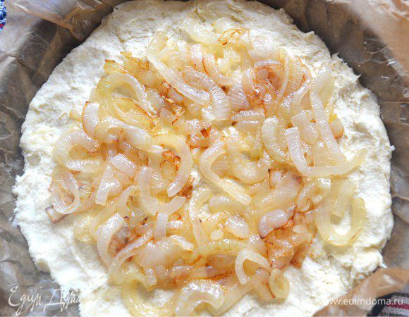 Поделить тесто на две части. Форму выстелить пекарской бумагой и смазать маслом. выложить дно пирога. Разложить жаренный лук равномерно отступая от края. 