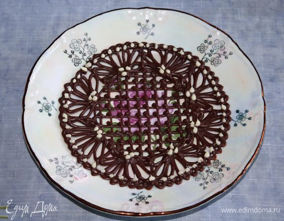 Даем блюдцу немного застыть, затем наносим капельки белого шоколада, который тоже надо растопить. Даем полностью застыть шоколаду при комнатной температуре. Затем осторожно перекладываем блюдце на сервировочную тарелку. 