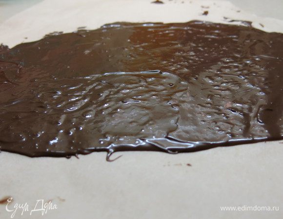 Перекладываем растопленный шоколад на пекарскую бумагу и длинным ножом расправляем в тонкий (2 мм) слой. В форме прямоугольника, приблизительно 28 см на 8 см. 