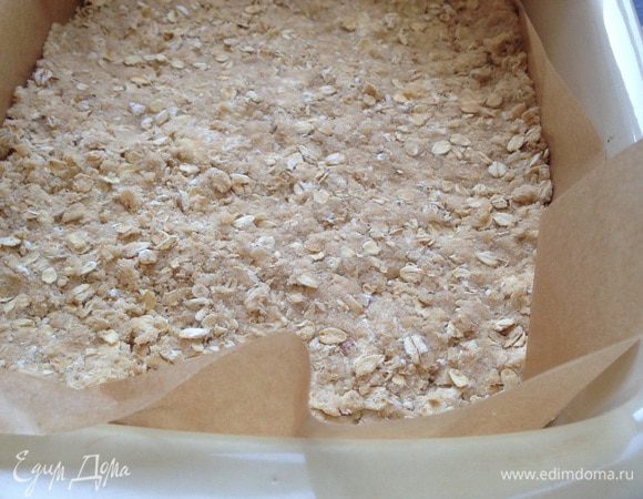 Форму застелить бумагой для выпечки так, чтобы края бумаги свисали на 2-3 см. Выложить на дно формы 2/3 мучной крошки. Равномерно распределить по дну и слегка придавить руками. 