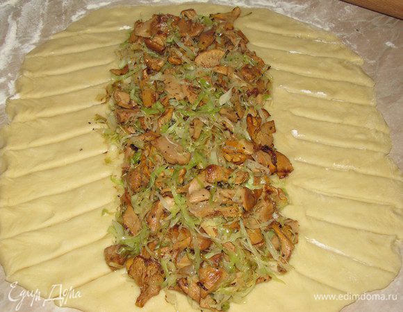 Подошедшее тесто раскатать в большой овал. Стол обязательно припылить мукой. Выложить начинку посередине. Свободные края теста разрезать на полоски острым ножом под углом примерно 45 градусов. 