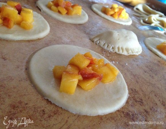 Тесто вынуть из холодильника, разделить на две части и раскатать в пласт толщиной 5мм. Вырезать формой кружочки. С одной стороны положить начинку из персиков, сформировать пирожок. Сначала края хорошо прижать пальцем, а затем по краю пройтись вилкой.