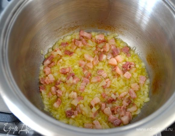 В кастрюле разогрейте сливочное масло и обжарьте на нем минуты 3-4 лук с беконом.