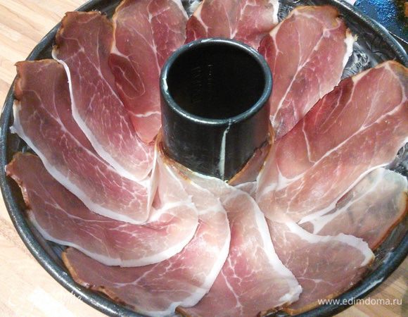 Форму (26 см в диаметре) смажьте маслом, выстелите тонкими ломтиками ветчины. Снаружи оберните форму фольгой. 