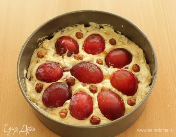 Выложите тесто в разъемную форму диаметром 20 см. Разрежьте пополам отложенные в сторону сливы, удалите косточки и выложите на пирог. Посыпьте пирог лесными орехами и слегка вдавите их в тесто.