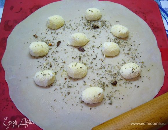 Разделить тесто на две части.
Большую часть раскатать в тонкий круг диаметром 30 см. Удобнее это делать на силиконовом коврике. Разложить на тесто подготовленный сыр, присыпать приправой (в моем случае – сушеные итальянские травки и сушеные помидоры).