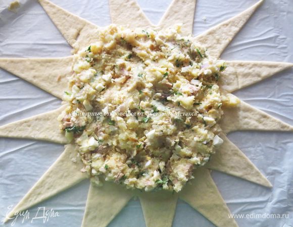 Из большой части также раскатываем лепешку, по диаметру на 12-15 см больше, чем верхняя и толщиной тоже чуть больше. Вырезаем треугольные края, для удобства назовем их "лучи". Обрезки теста собираем в ком и накрываем (нам они пригодятся для оформления).
В середину лепешки, равномерным слоем выкладываем начинку.