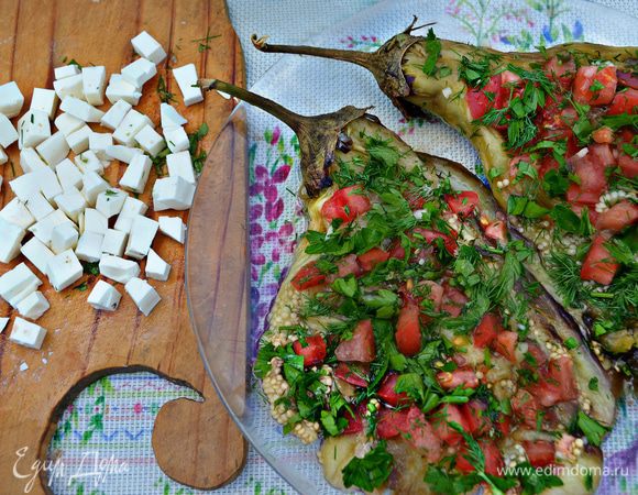На баклажаны выложить чеснок, помидоры, рубленную зелень и нарезанную кубиками фету. Вместо феты можно использовать брынзу или адыгейский сыр, также вы можете не нарезать кубиками, а покрошить поверх помидоров.