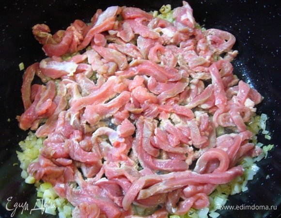 Мясо нарезать поперек волокон брусочками. 
Лук, чеснок измельчить.
Помидор нарезать кубиком.
Разогреть в сотейнике с толстым дном оливковое масло.
Обжарить лук и чеснок до прозрачности.
Добавить к овощам мясо, обжарить.
