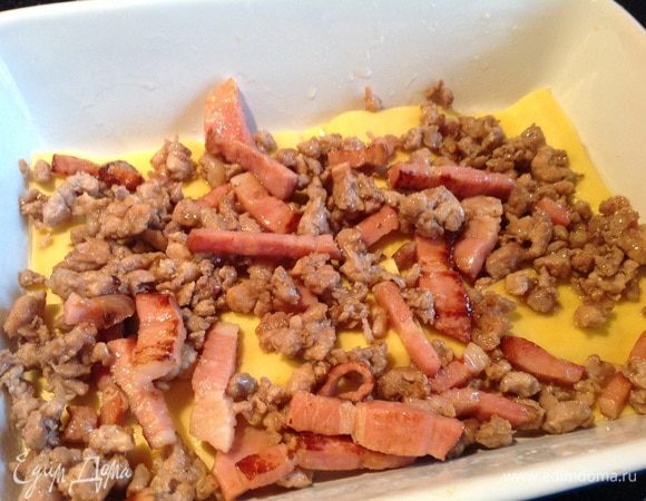Форму для запекания смажьте маслом, выложите 3 листа лазаньи, сверху половину начинки из фарша и бекона.