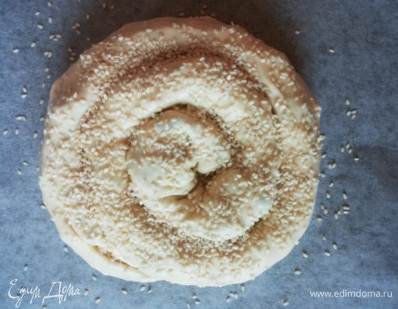 Получившуюся колбаску обильно смазываем оливковым маслом и перекладываем на противень, застеленный пергаментом, в форме спирали. Посыпаем кунжутом. 