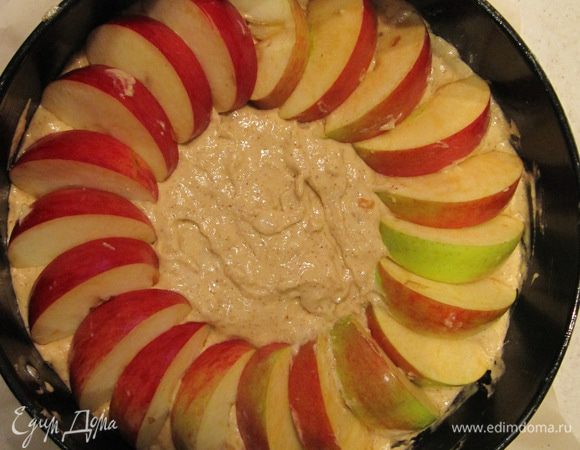 Дно разъемной формы (у меня диаметром 22 см) выстелить пергаментом. Форму смазать небольшим количество сливочного масла. Выложить тесто, разровнять. 
Яблоки разрезать на четвертинки, удалить сердцевины. Каждую четвертинку разрезать еще на три части. Дольки яблок уложить по внешнему кругу пирога веером. Отправить форму в предварительно разогретую до 180C духовку на 40-50 мин. Время выпекания зависит от вашей духовки. Если центр пирога будет зарумяниваться слишком быстро, то за 10 мин до готовности пирога накрыть форму фольгой.