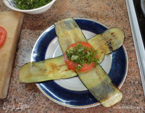 По два язычка из баклажана сложить крестом (обжаренной стороной вверх), на середину положить колечко помидора, затем зелень с чесноком,