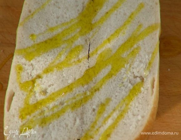 Багет разрезать вдоль пополам, сбрызнуть оливковым маслом и дать ему впитаться.