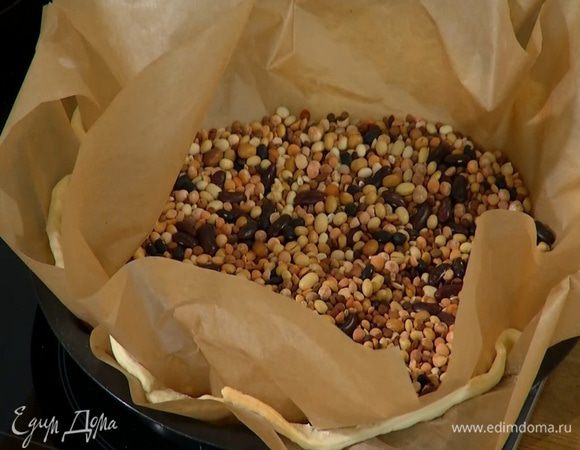 Накрыть тесто вторым листом для выпечки, насыпать сверху горох или фасоль и отправить в разогретую духовку на 10‒12 минут.