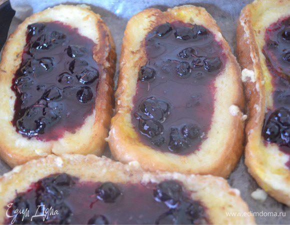 Поджаренные гренки выложить на противень, застеленный промасленной бумагой для выпечки. На каждую гренку положить по 1 ст. ложке черничного джема. Можно джем заменить на свежие ягоды или нарезанные фрукты, это как Вам ваша фантазия подскажет.
