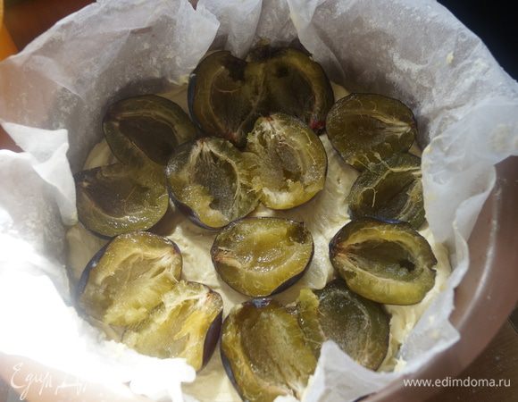 Сливы разрезать пополам и удалить косточку. Форму для выпечки застелить пергаментом и выложить 1/2 часть теста, затем поместить сливы 