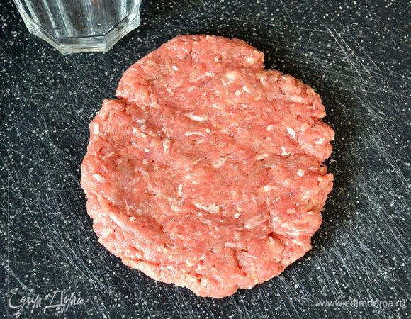 Возьмите часть фарша (100-120 г) и, положив на доску, сформируйте ладонью такую лепешку.