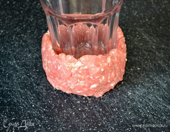 Возьмите стакан (подойдет бокал для пива, дно 6 см в диаметре). Смочите дно стакана в холодной воде и поставьте его ровно посередине мясной лепешки. 
Мокрыми руками сформируйте вокруг бокала бортики (в начале может показаться, что фарш не хочет приставать к бокалу, но он и не должен именно "пристать" к нему. Поэтому, просто помогая себе обеими руками, сформируйте подобие чашечки из фарша - все получается отлично!).