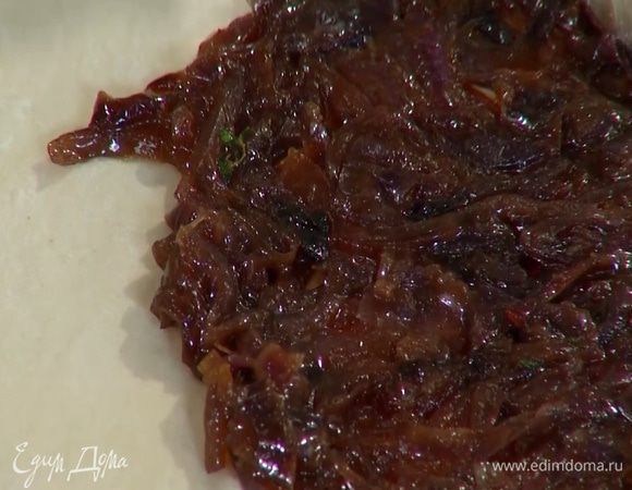 Противень выстелить бумагой для выпечки, выложить тесто, сверху равномерно распределить карамелизированный лук, отступая от краев, чтобы остались бортики.