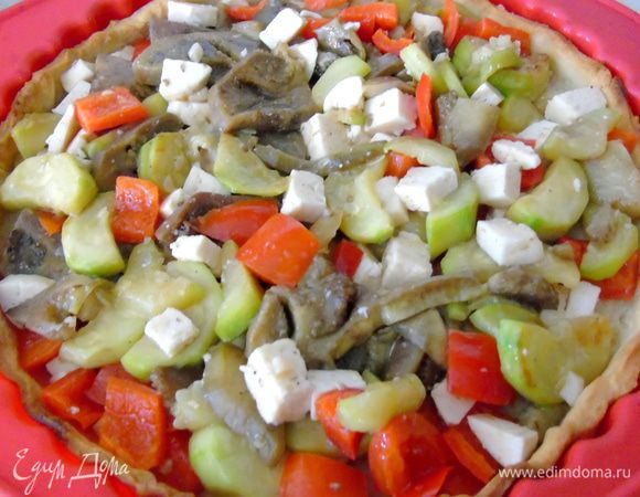 Фету поломать или нарезать кусочками. Добавить к овощам, перемешать, посолить, поперчить, выложить в полувыпеченную основу.