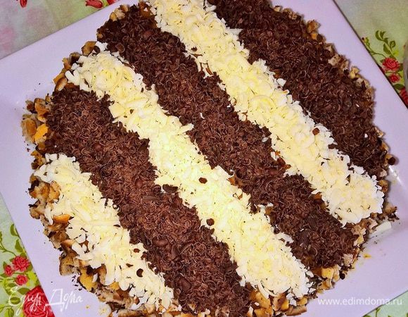 Готовые охлажденные коржи разрезаем по горизонтали, переслаиваем их кремом. Также промазываем бортики и верхушку. Орехово-шоколадной смесью, указанной в предыдущем шаге, посыпаем бока торта. Затем оформляем верх десерта стружкой из темного и белого шоколада. 