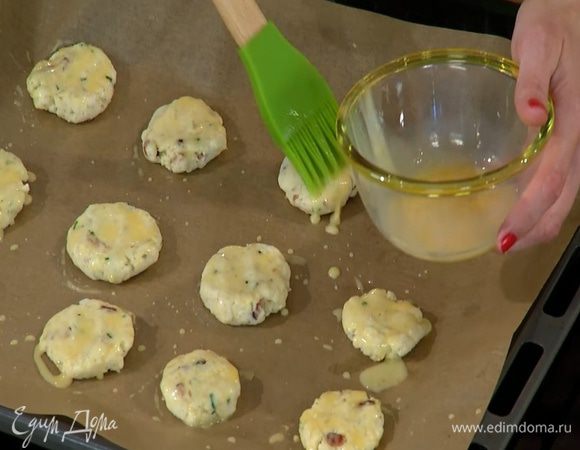 Из теста сформировать небольшие лепешки, выложить их на выстеленный бумагой для выпечки противень и смазать желтком с молоком.