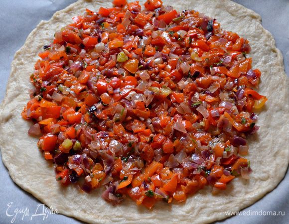 На противень выложите пекарскую бумагу. Тесто раскатайте в круг толщиной 1,5-2 см, пальцами разомните края, чтобы они были тоньше середины.
Распределите по поверхности теста соус, не доходя до края 3 см. 
