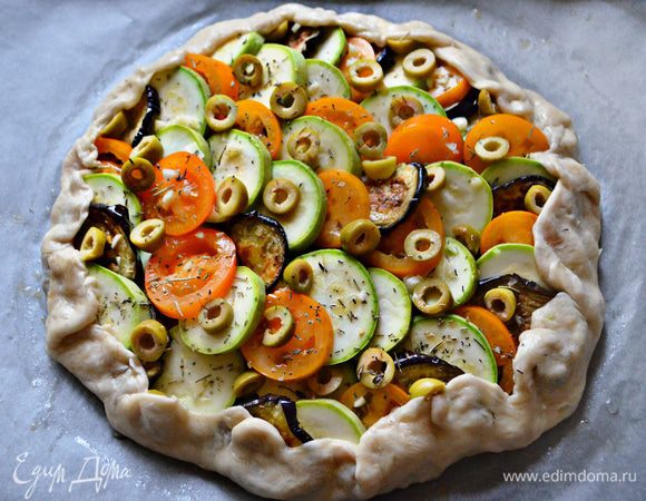 Сверху соуса разложите, чередуя ломтики овощей. Приправьте солью, посыпьте рубленным чесноком, прованскими травами, перцем, разложите порезанными на кружочки оливками. Приподнимите края теста, прикрывая ими начинку. Поставьте запекаться в духовку на 35-45 мин при 180г.

