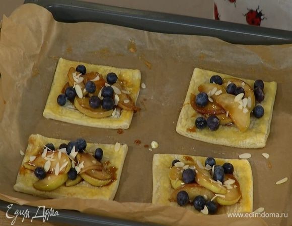 Подпеченное тесто вынуть из духовки, в центр каждого квадратика выложить карамелизированные яблоки, присыпать их голубикой и миндалем.