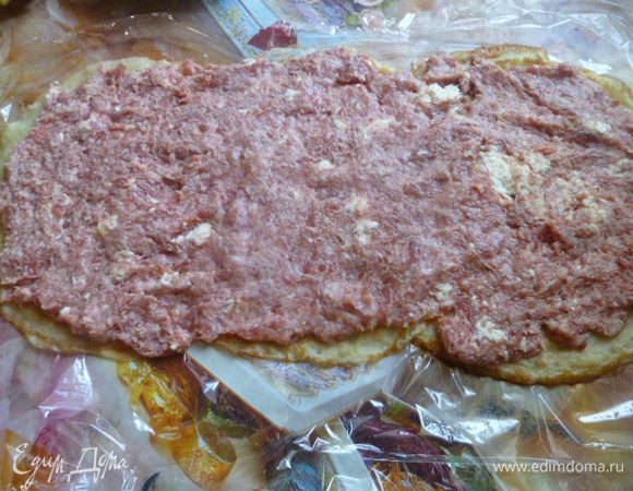 На пищевую пленку внахлест выложить три блина, выложить ровным слоем на них половину фарша.