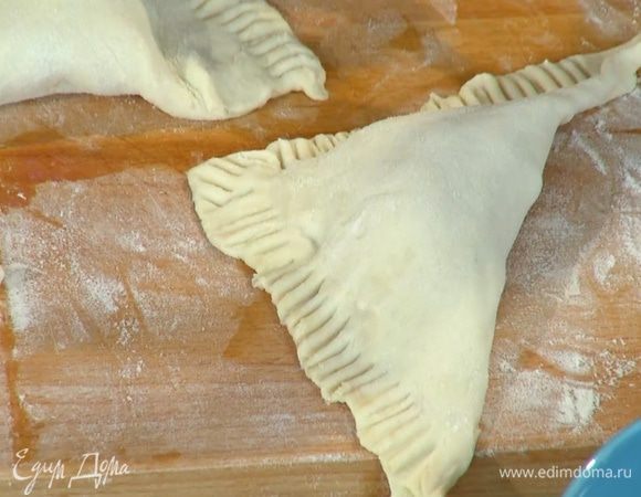 Смазать края теста яичным белком, накрыть начинку свободным углом теста так, чтобы получились треугольники, и прижать края сначала руками, затем вилкой (неровные края можно срезать ножом).