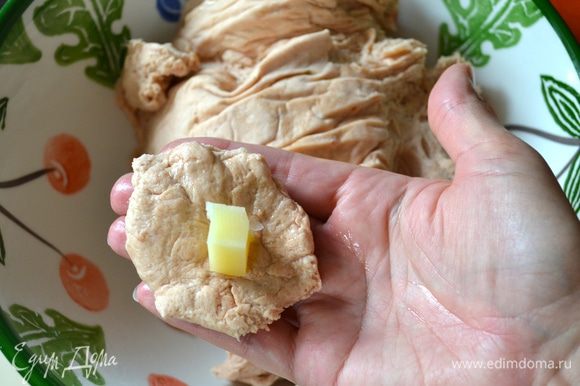 Ладони также смазать маслом. Теперь, отщипывая от теста по кусочку теста размером с грецкий орех, формировать маленькие булочки. Тесто слегка расплющить и в центр положить кусочек сыра.