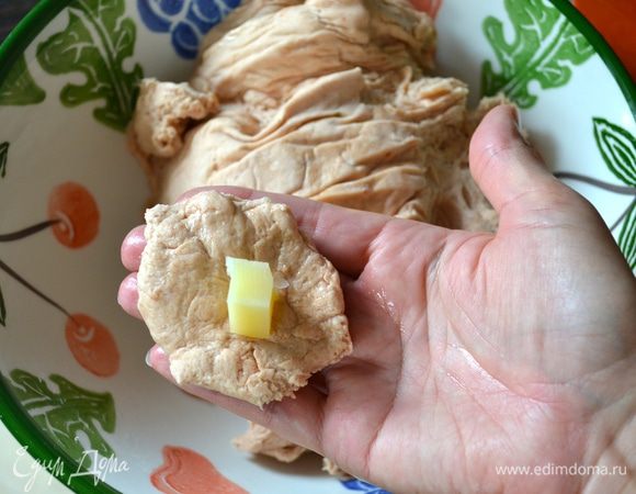 Ладони также смазать маслом. Теперь, отщипывая от теста по кусочку теста размером с грецкий орех, формировать маленькие булочки. Тесто слегка расплющить и в центр положить кусочек сыра.
