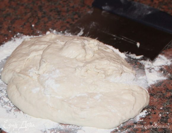 Самый "противный" процесс - это начало. Смешиваем все ингредиенты и замешиваем. Получаем ползучую смесь, которая сильно липнет к рукам. Нельзя их ничем ни смачивать, ни присыпать мукой. Присыпаем мукой поверхность стола и выкладываем наше тесто. Я на первом этапе работаю с кондитерским скребком. У меня металлический, но лучше пластиковый или силиконовый. При помощи скребка переворачиваем тесто до тех пор, пока оно не вберет в себя ту муку, что мы присыпали на стол.