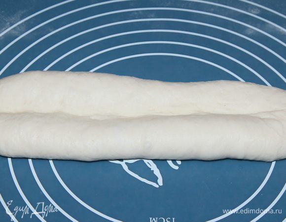 Ребром ладони продавим неглубокий желобок вдоль середины получившегося продолговатого куска теста. Затем берем одну половинку теста сворачиваем и как бы заворачиваем его в эту ложбинку. Тоже самое делаем со второй частью. Снова продавливаем ложбинку посередине вдоль большей стороны. 
