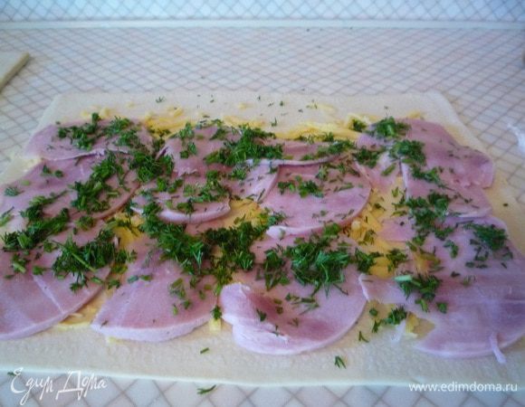 На прямоугольный пласт теста распределить сыр, поверх сыра уложить пластинки ветчины и щедро посыпать укропом.