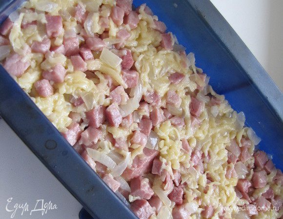 Глубокую форму смазать сливочным маслом (силиконовую можно не смазывать) и выложить ровным слоем половину картофельной смеси. Сверху распределить бекон с сыром и луком.