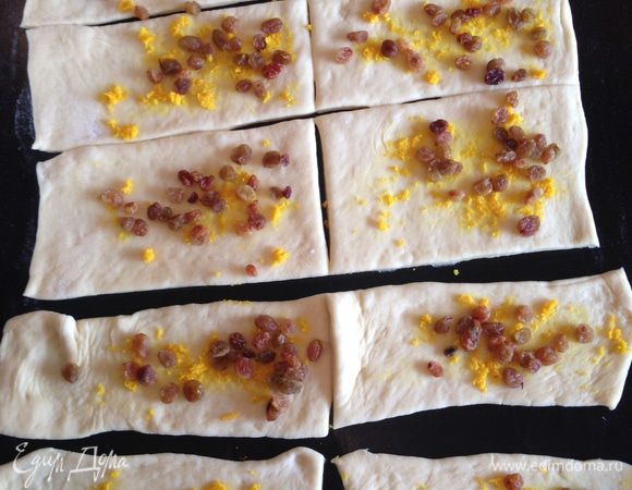 Натираем цедру апельсина (сам апельсин нам не понадобится).
Смазываем тесто маслом и посыпаем равномерно сахаром каждый кусочек, затем раскладываем цедру и изюм.