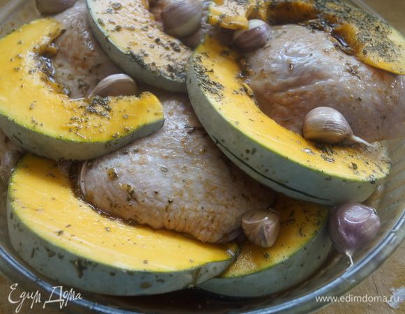 После того, как тыква настоится, выложить ее к куриным бедрышкам в форму, поверх положить вымытые неочищенные дольки чеснока, немного посолить.