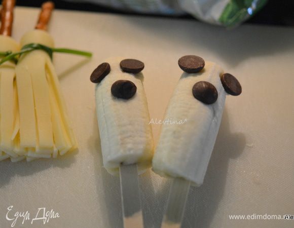 Приготовить стакан подставку для банана. Банан спелый разрезать на 2 части.  Воткнуть палочку в центр мякоти снизу. Снять кожуру. Распределить шоколадные капли, как глаза и нос, смотрите фото. Конфетами по тематике можно дополнить детали.
