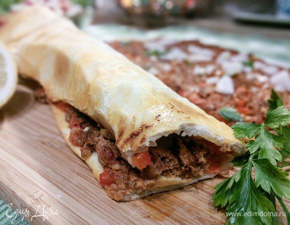 В это время нарезать мелко маленькую луковицу, зубок чеснока  и петрушку, посыпать ими пиццу, сбрызнуть лимонным соком и свернуть в рулет. 