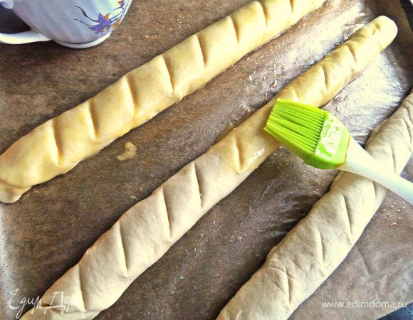 Раскладываем заготовки на смазанный маслом пергамент на противне. Делаем надсечки ножом,смазываем взбитым яйцом кисточкой.